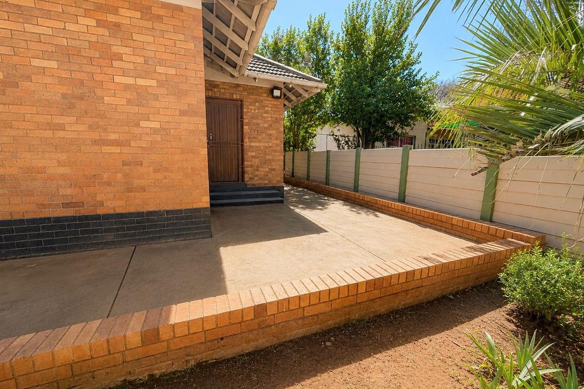 A rear exterior view featuring a face brick facade, a concrete patio area, and a secure precast boundary wall.