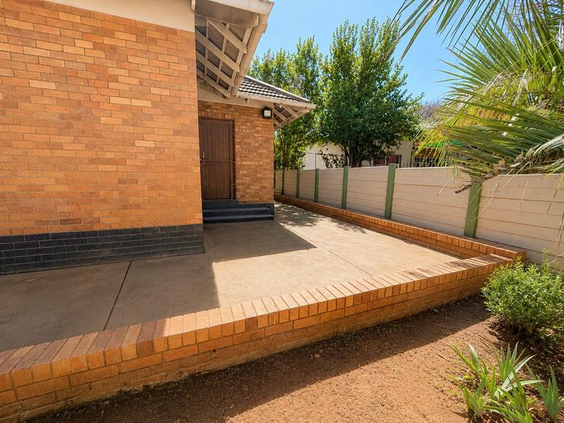 A rear exterior view featuring a face brick facade, a concrete patio area, and a secure precast boundary wall.