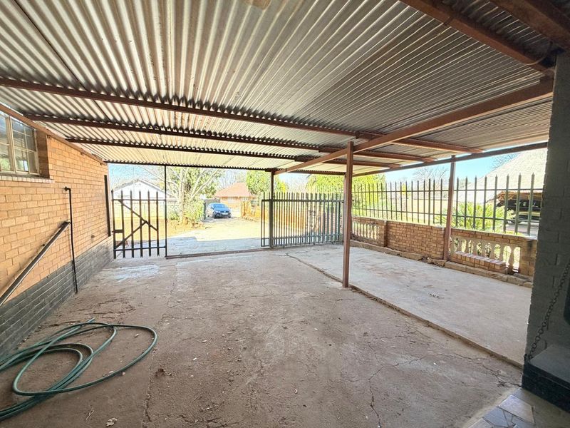 A functional open-sided garage or carport featuring a corrugated metal roof, concrete flooring, and secure perimeter fencing.