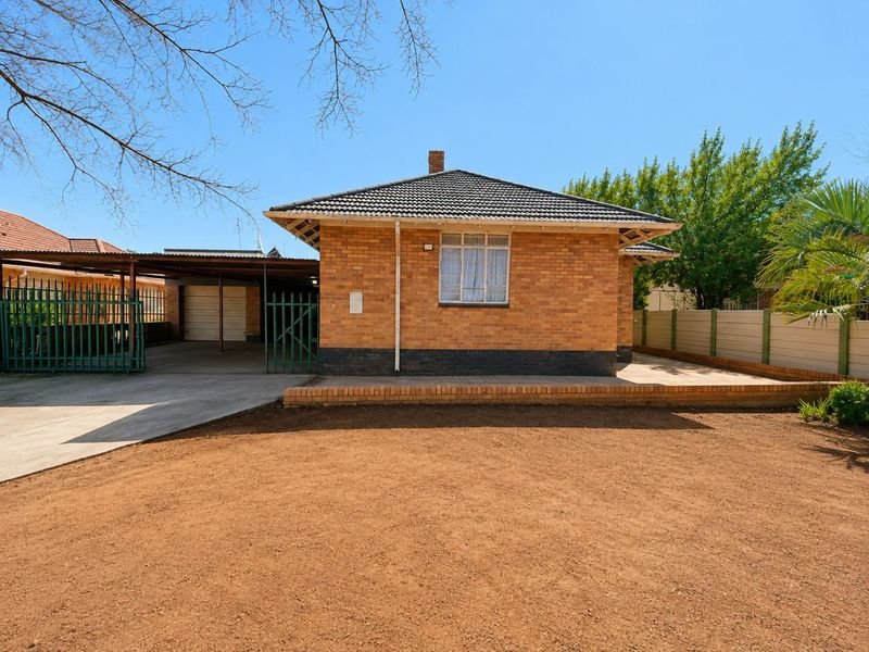 Front view of a single-story brick house featuring a tiled roof, attached carport, and a large open yard area.