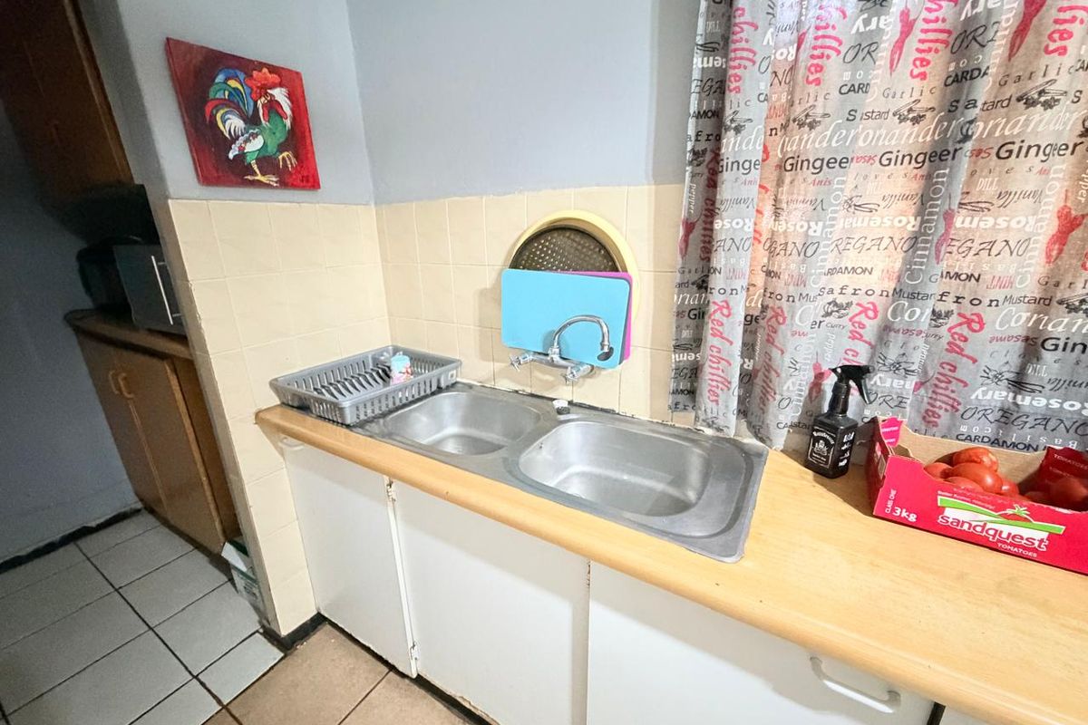 A functional kitchen area featuring a double bowl stainless steel sink, tiled splashback, and built-in cabinetry with laminate countertops.