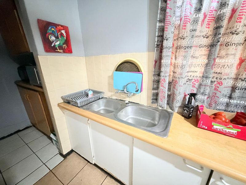 A functional kitchen area featuring a double bowl stainless steel sink, tiled splashback, and built-in cabinetry with laminate countertops.