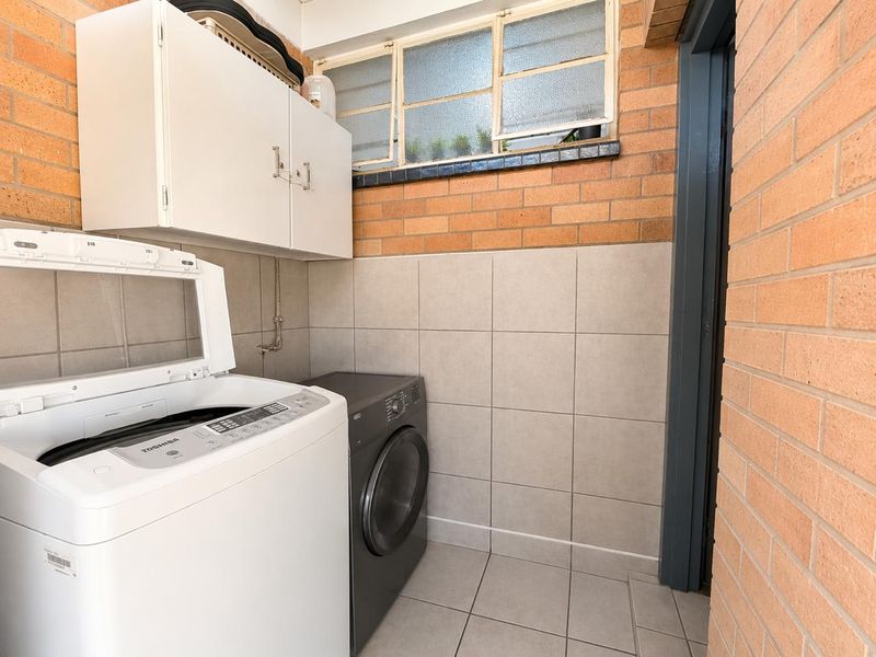 Functional laundry area featuring exposed brick walls, tiled flooring, wall-mounted cabinetry, and a louvered window for ventilation.