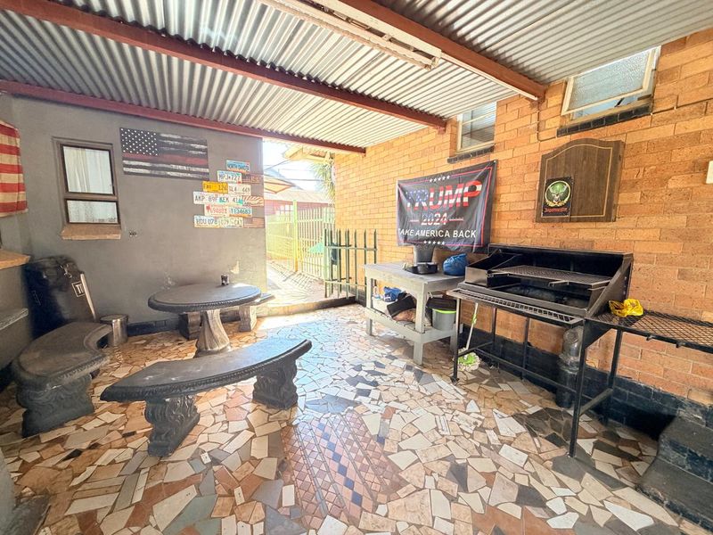 Covered outdoor patio area featuring exposed brick walls, a built-in braai, and tiled flooring, providing a functional space for outdoor entertaining.