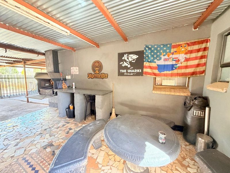 Covered outdoor patio area featuring a built-in braai, stone tile flooring, and a concrete counter, providing a functional space for outdoor entertaining.
