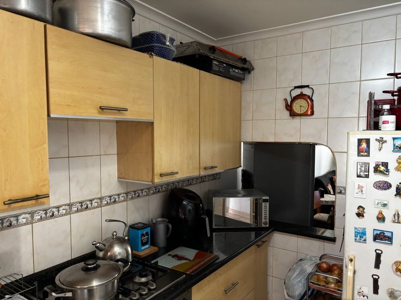 A functional kitchen featuring light wood cabinetry, dark granite countertops, a gas hob, and a tiled backsplash with decorative border detailing.