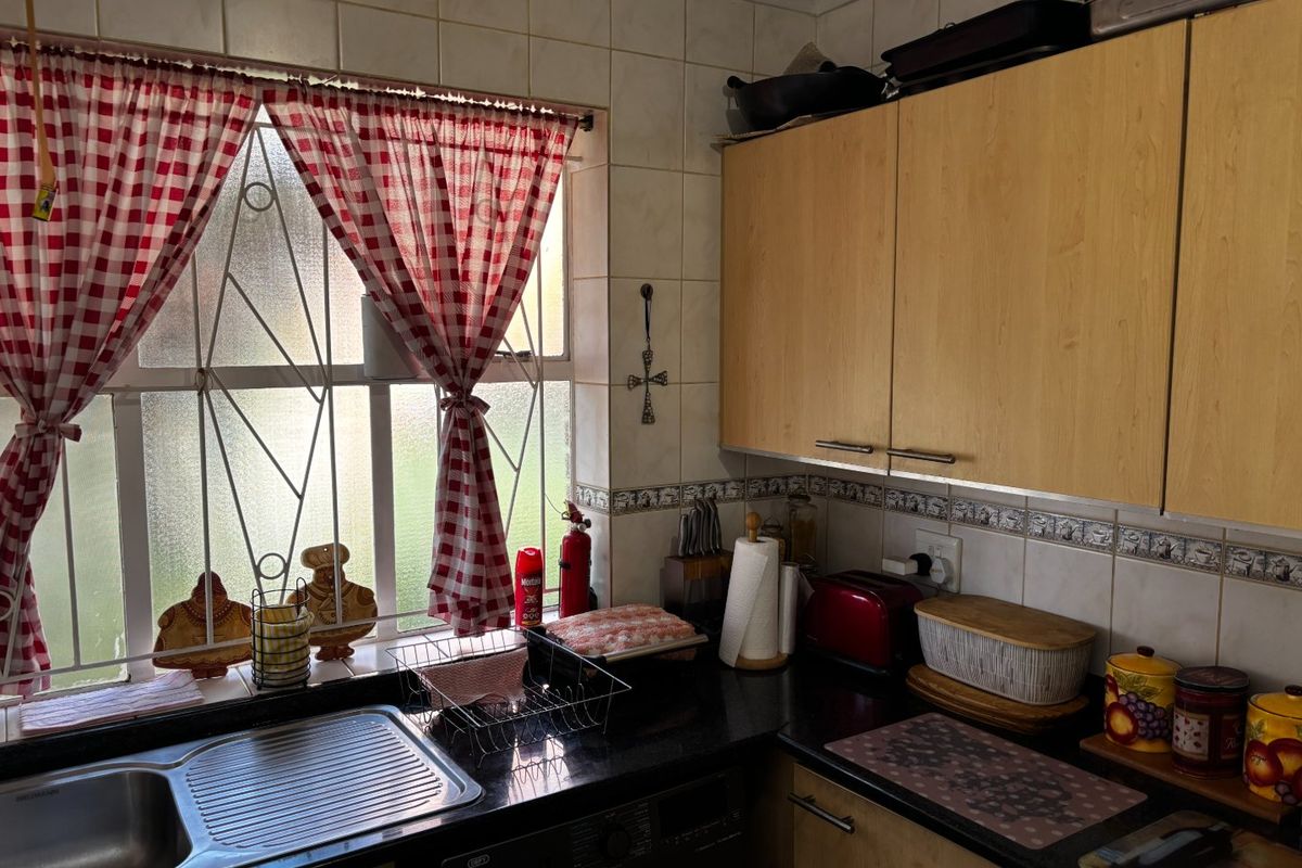 A functional kitchen featuring laminate cabinetry, granite countertops, and a stainless steel sink, with tiled backsplash and security bars on the window.