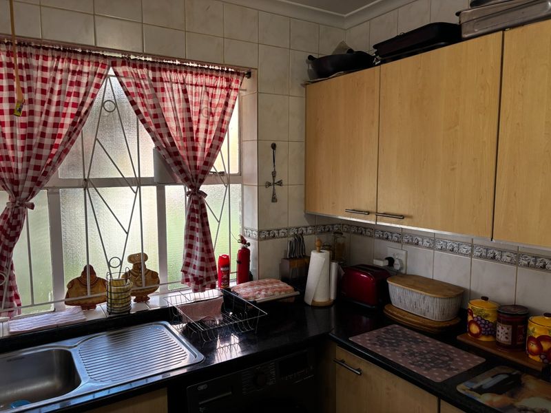 A functional kitchen featuring laminate cabinetry, granite countertops, and a stainless steel sink, with tiled backsplash and security bars on the window.