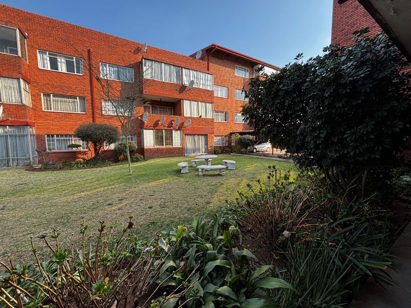 A view of the rear exterior of the apartment complex, featuring a well-maintained communal garden and lawn area with brick building facades.