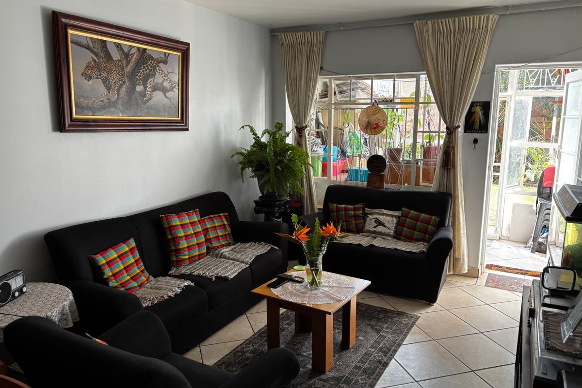 A comfortable living room featuring tiled flooring, large windows with curtain rails, and direct access to an outdoor patio area.