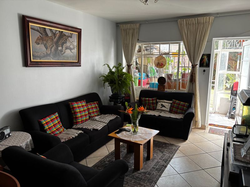 A comfortable living room featuring tiled flooring, large windows with curtain rails, and direct access to an outdoor patio area.