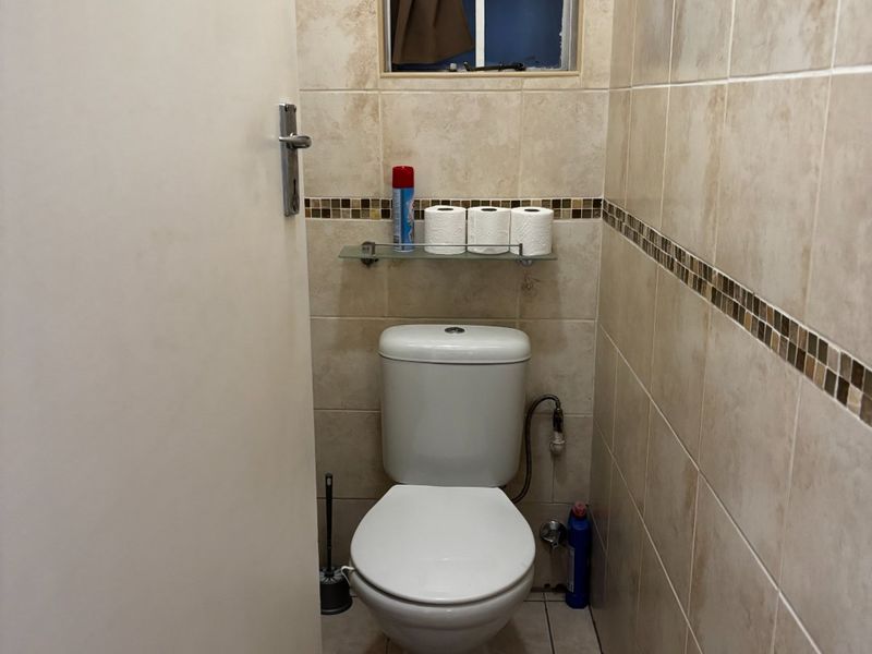 A compact bathroom featuring neutral ceramic wall and floor tiles, a standard toilet, and a small window for ventilation.