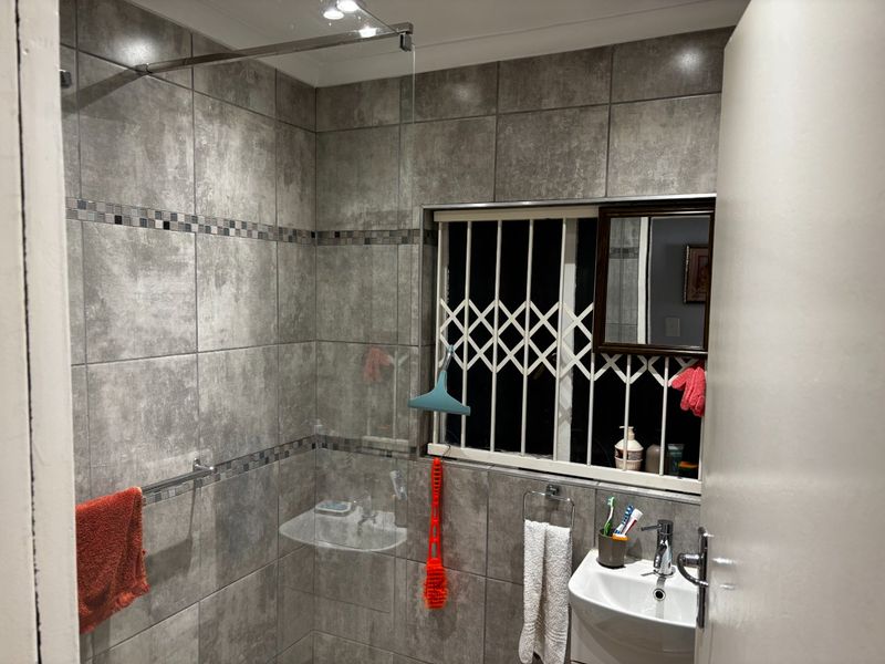 A modern bathroom featuring grey stone-look wall tiles, a glass shower screen, and a pedestal basin with a chrome mixer tap.