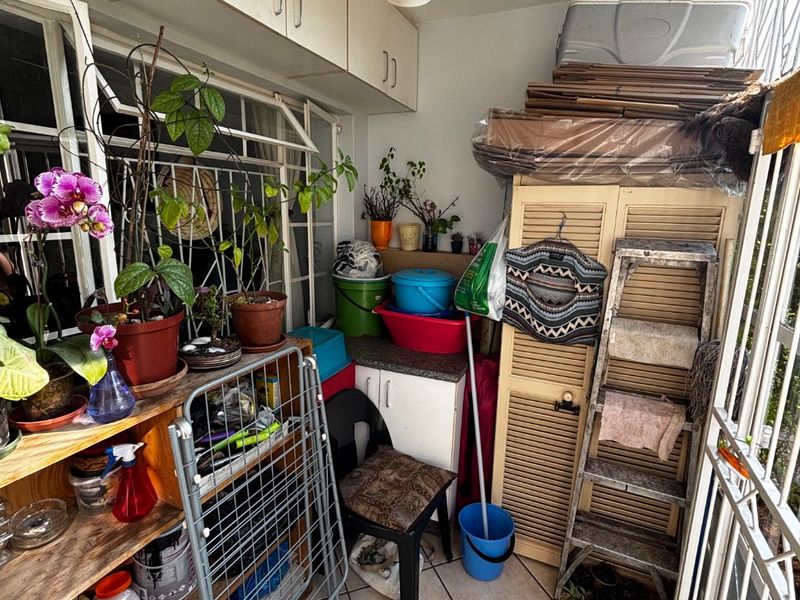 Enclosed balcony or utility area featuring overhead storage cabinetry, tiled flooring, and security bars, currently utilized for storage.
