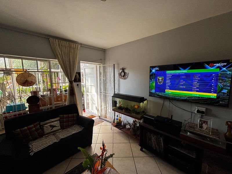 A comfortable living room featuring tiled flooring, a large window with natural light, and a wall-mounted television setup.