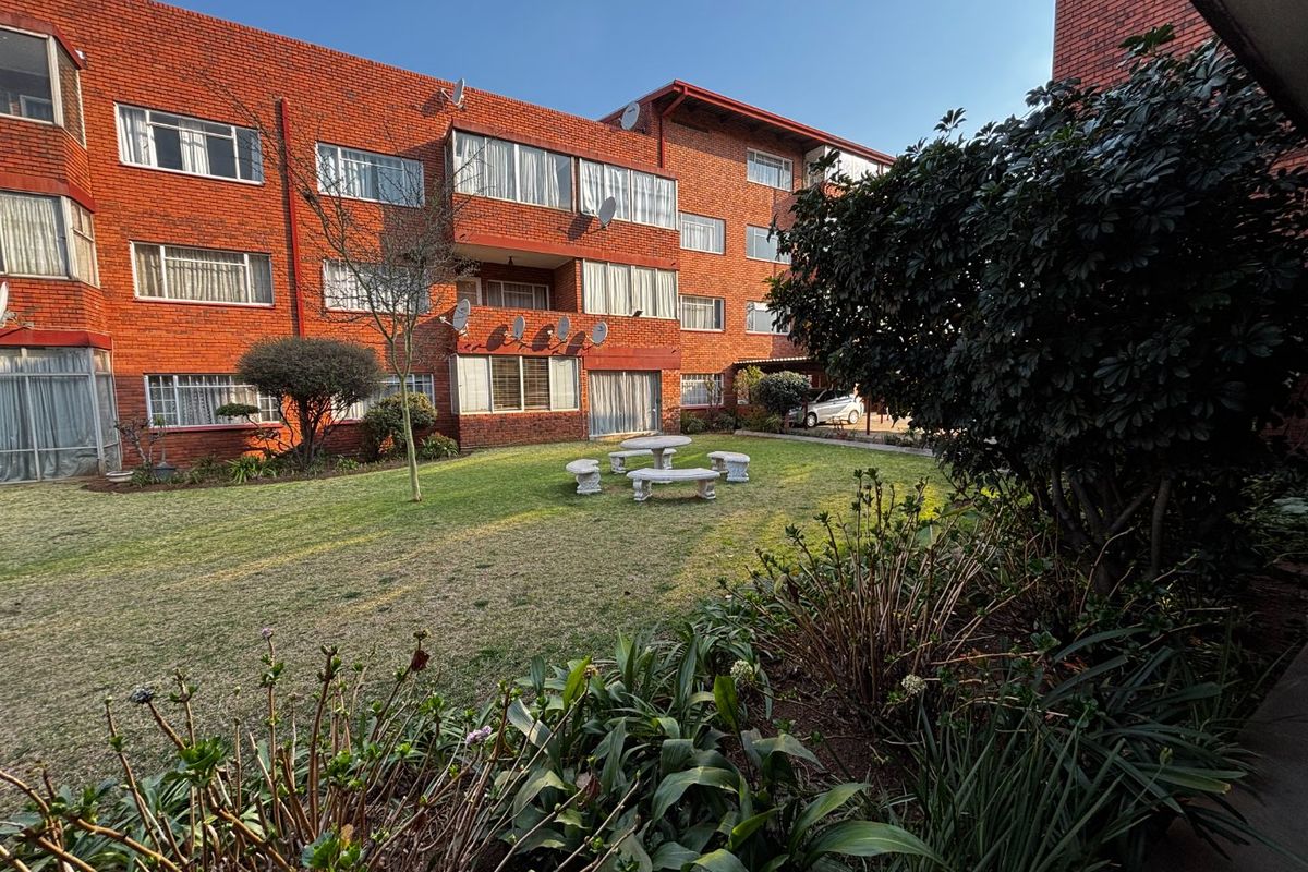 A view of the rear exterior of the apartment complex, featuring a well-maintained communal garden area and face brick building facade.