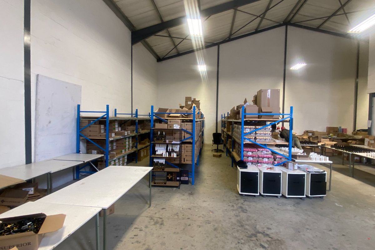 Commercial warehouse space featuring high ceilings with exposed steel trusses, concrete flooring, and industrial steel racking units for storage.