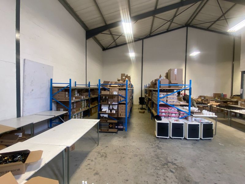 Commercial warehouse space featuring high ceilings with exposed steel trusses, concrete flooring, and industrial steel racking units for storage.
