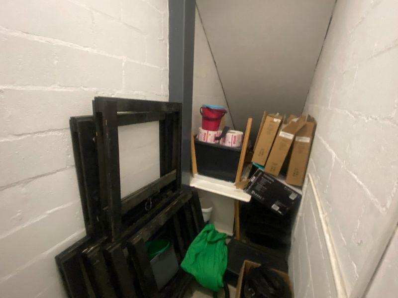 A small utility storage space located under a staircase, featuring painted brick walls and a sloped ceiling.