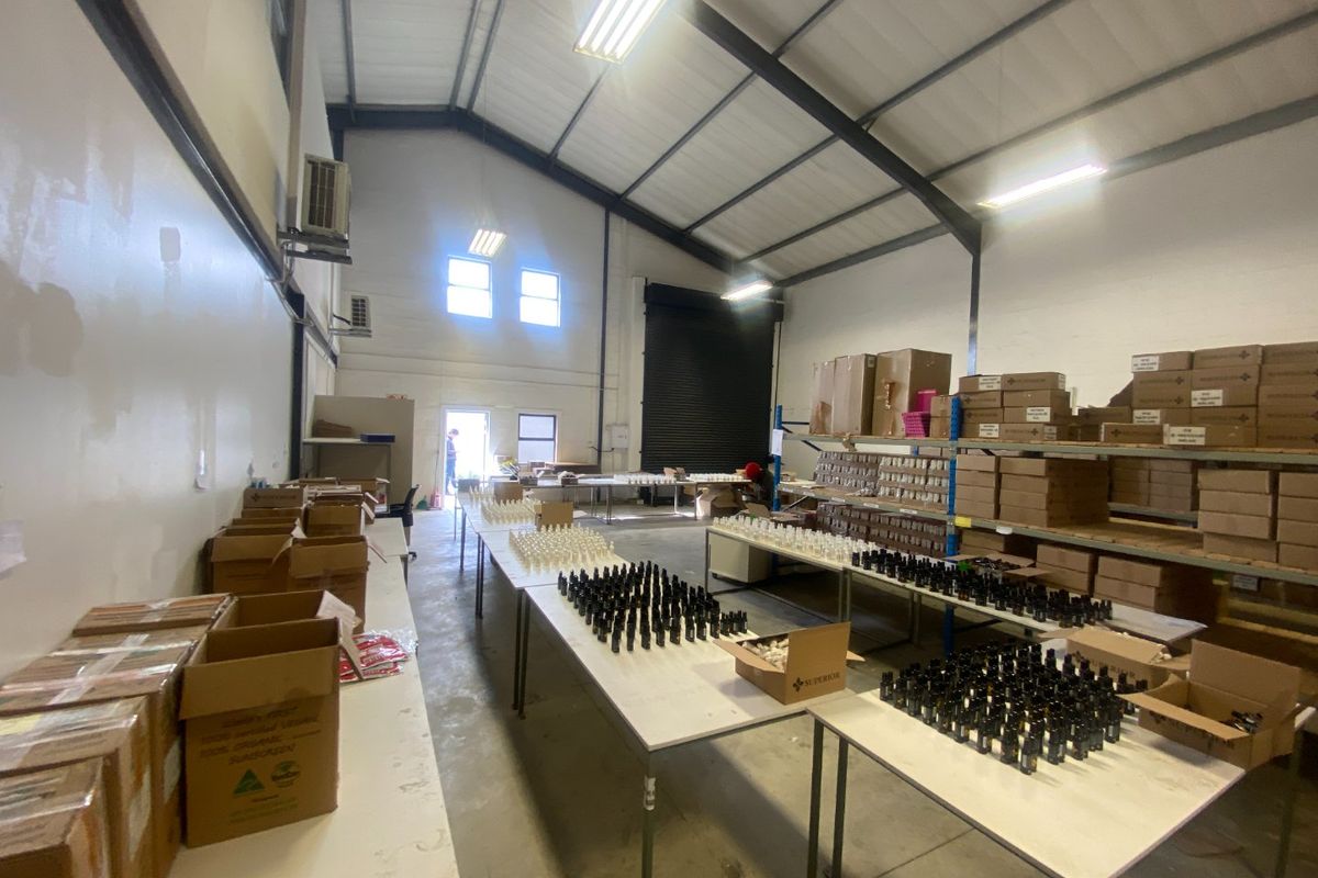A functional commercial warehouse or utility space featuring high ceilings with exposed steel rafters, roller shutter access, and industrial fluorescent lighting.