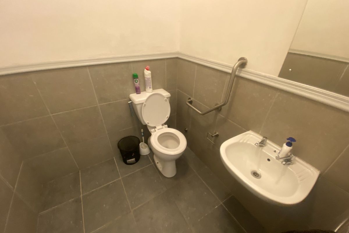 A functional commercial bathroom featuring tiled walls and flooring, a wall-mounted sink, and accessibility grab rails.