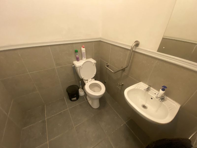 A functional commercial bathroom featuring tiled walls and flooring, a wall-mounted sink, and accessibility grab rails.
