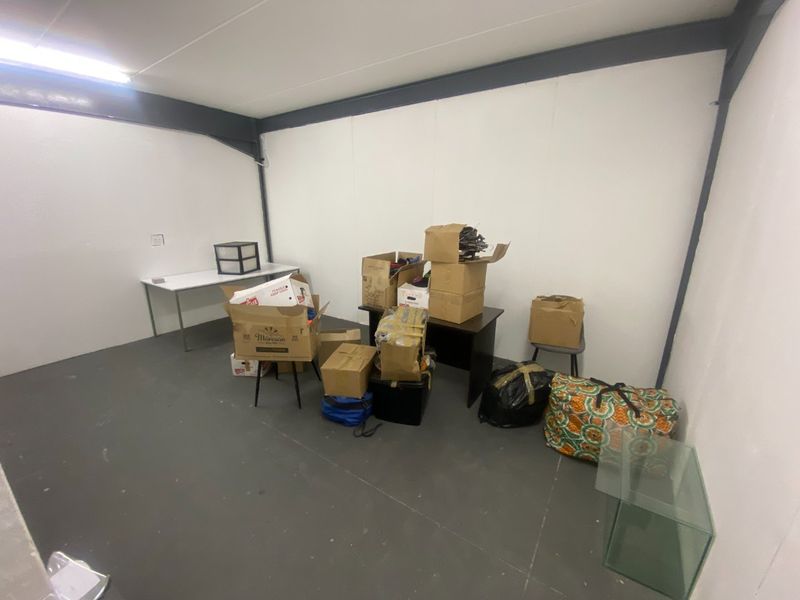 A functional utility space featuring white walls, exposed steel structural beams, and overhead fluorescent lighting, suitable for storage or workspace use.