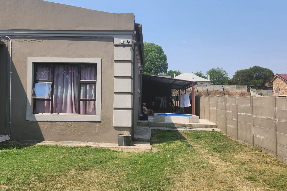 Rear view of the property featuring a small swimming pool, covered patio area, and a precast concrete boundary wall enclosing the garden.