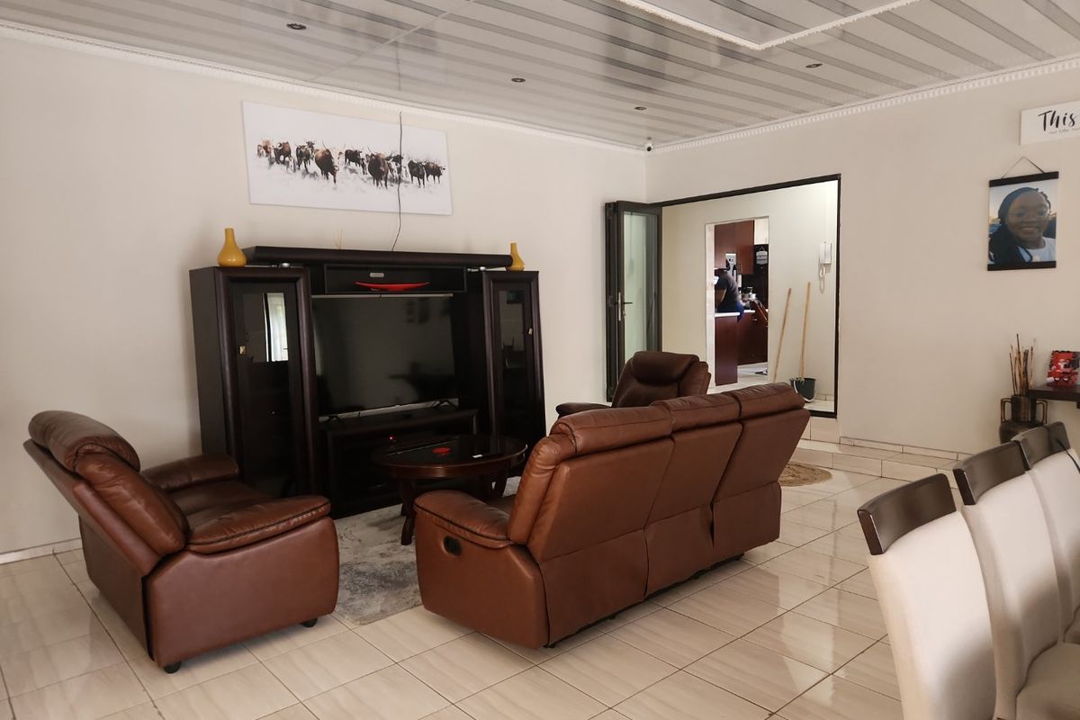 A spacious living room featuring tiled flooring, decorative ceiling panels with recessed lighting, and a neutral wall finish.