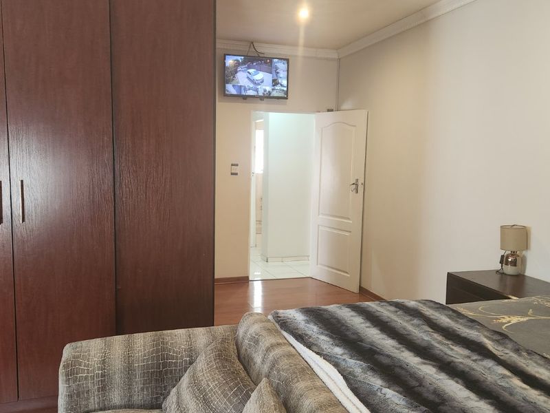 A bedroom featuring dark wood built-in wardrobes, laminate flooring, and decorative ceiling coving, with an adjacent doorway leading to an adjoining room.