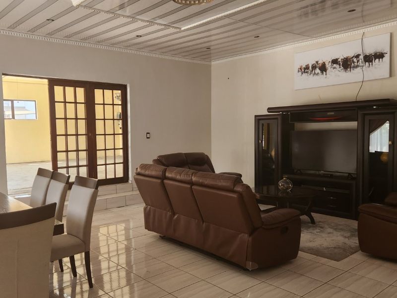 Spacious open-plan living and dining area featuring polished tile flooring, a decorative coffered ceiling with recessed lighting, and direct access to the patio.