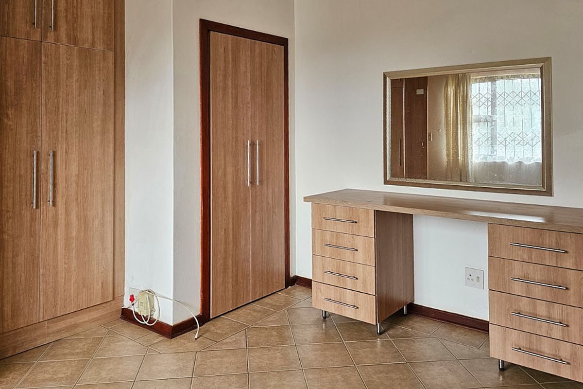 A bedroom featuring built-in wooden cupboards and a matching built-in vanity unit with drawers, set against tiled flooring.