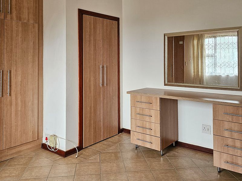 A bedroom featuring built-in wooden cupboards and a matching built-in vanity unit with drawers, set against tiled flooring.