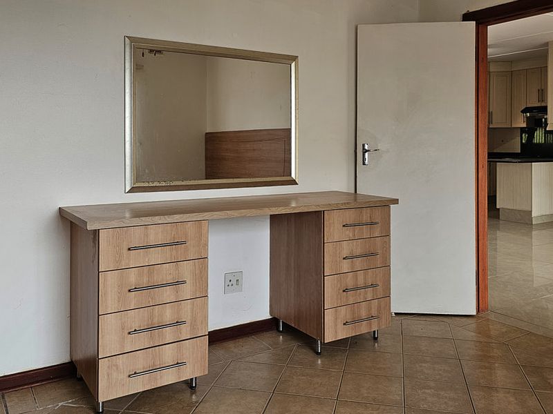 A bedroom featuring tiled flooring and a built-in vanity unit, with a view through the doorway into the adjacent kitchen area.