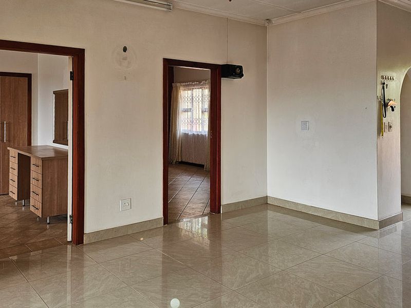 An open-plan living area featuring neutral tiled flooring, wooden door frames, and an arched entryway leading to the exterior.