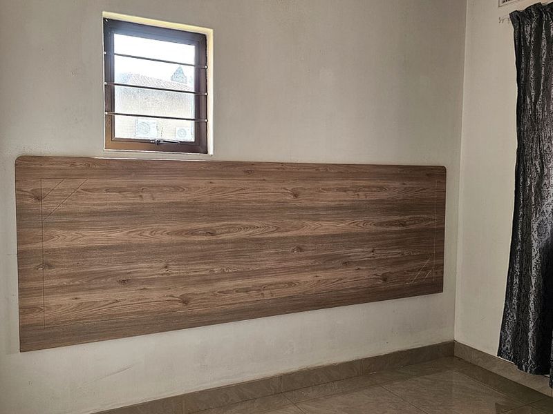 A bedroom featuring tiled flooring and a built-in wood-look headboard mounted on the wall beneath a small window with security bars.