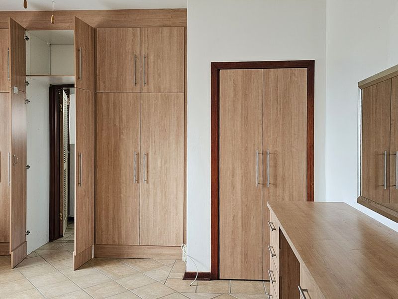 A bedroom featuring extensive built-in wooden cabinetry, a matching built-in vanity, and neutral tiled flooring.