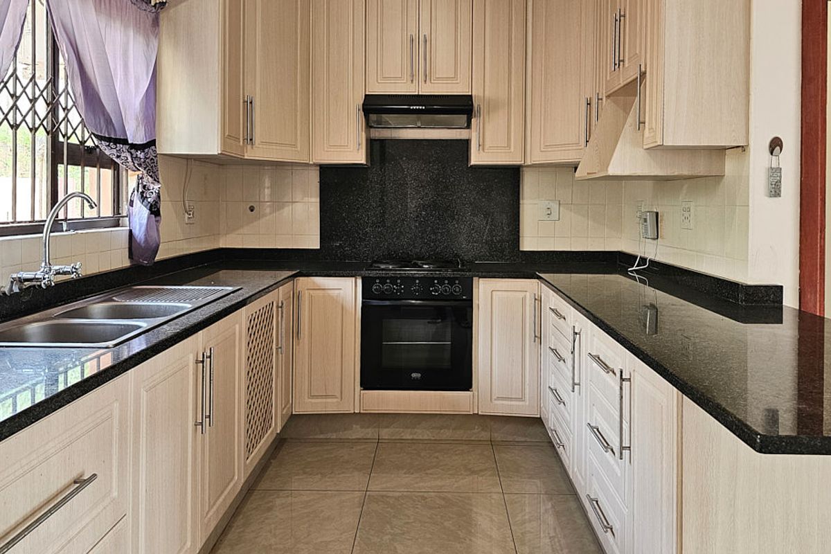 A functional kitchen featuring light wood-finish cabinetry, dark granite countertops, a built-in oven with hob, and tiled flooring.
