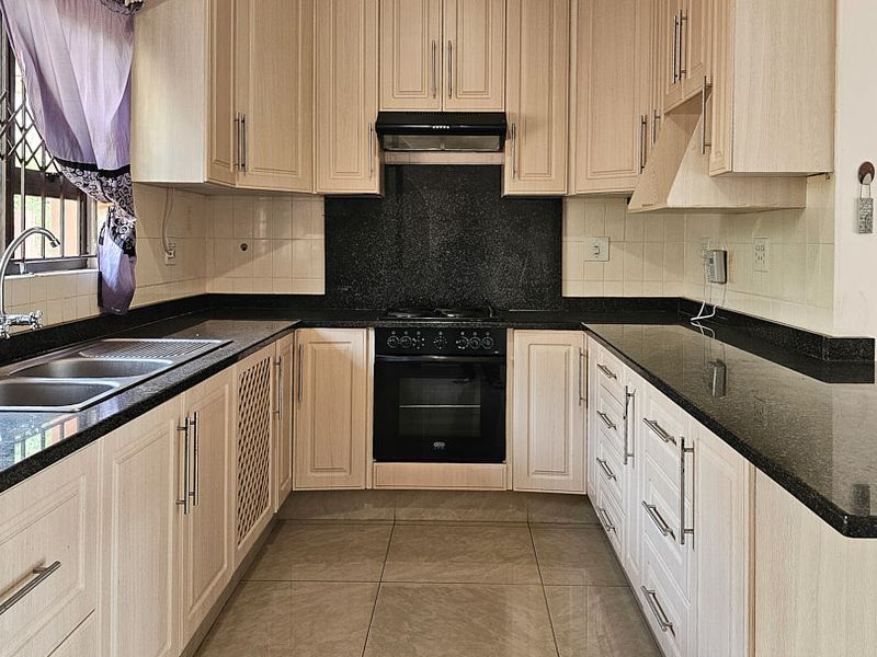 A functional kitchen featuring light wood-finish cabinetry, dark granite countertops, a built-in oven with hob, and tiled flooring.
