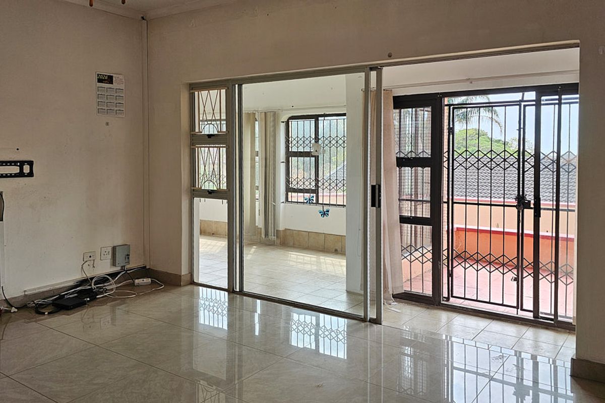 Spacious living area featuring tiled flooring and large sliding glass doors that open onto an enclosed patio with security gates.