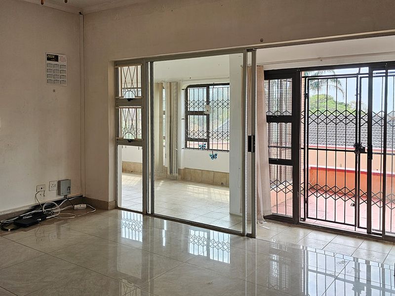 Spacious living area featuring tiled flooring and large sliding glass doors that open onto an enclosed patio with security gates.