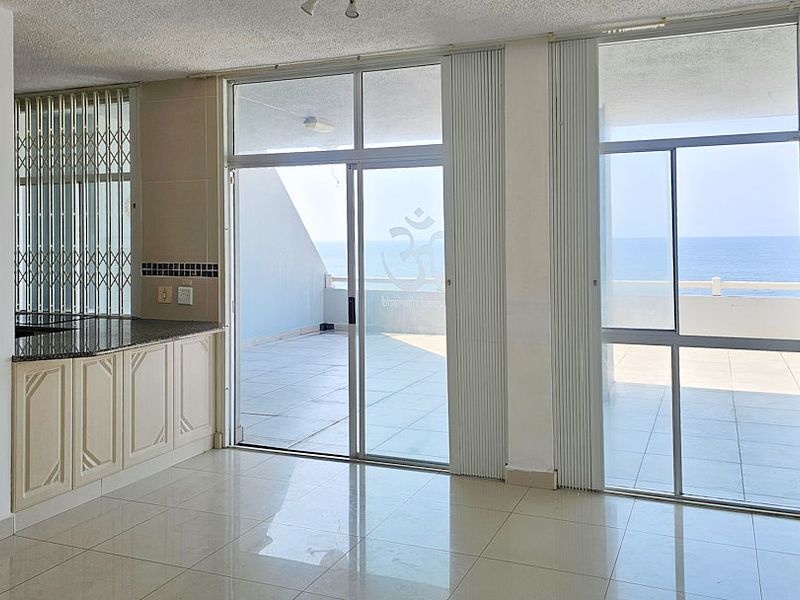 Open-plan kitchen and living area featuring tiled floors, granite countertops, and large sliding glass doors leading to a spacious balcony with ocean views.