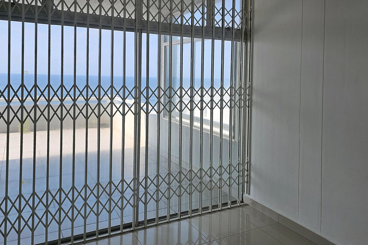 An empty living area featuring tiled flooring and a sliding glass door with a security gate, offering a view of the ocean.