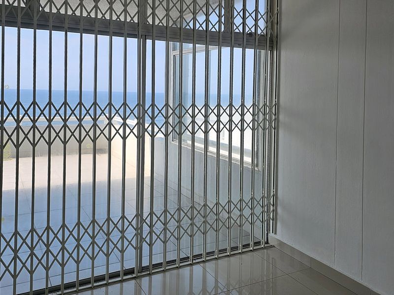 An empty living area featuring tiled flooring and a sliding glass door with a security gate, offering a view of the ocean.