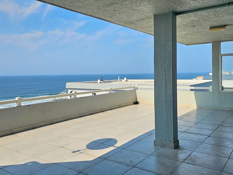 A spacious, open-air balcony featuring tiled flooring and a concrete support pillar, offering expansive, unobstructed views of the ocean.