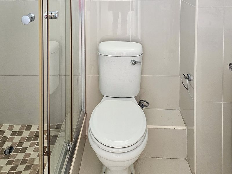 A functional bathroom featuring a tiled shower enclosure, a standard toilet, and a vanity basin with neutral wall and floor tiling.