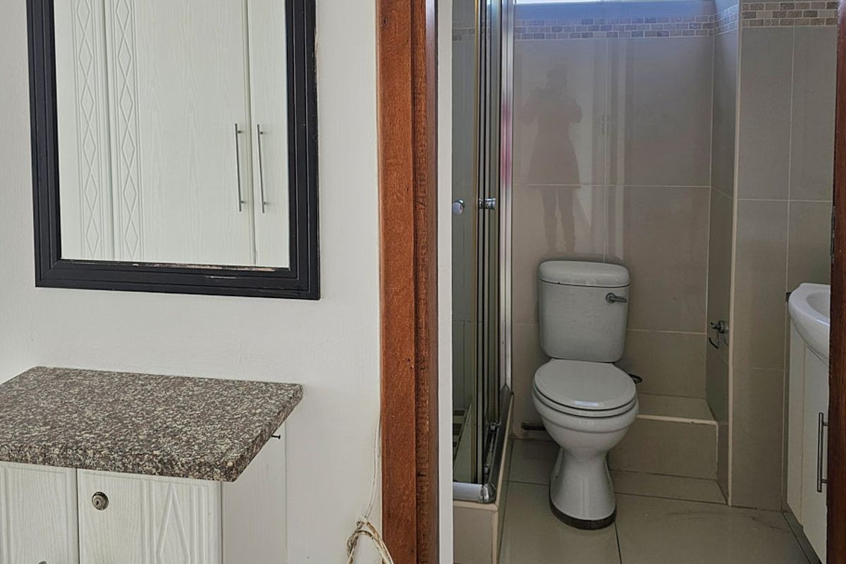 A functional bathroom featuring a shower enclosure, toilet, and vanity unit with a granite countertop, finished with neutral wall and floor tiles.