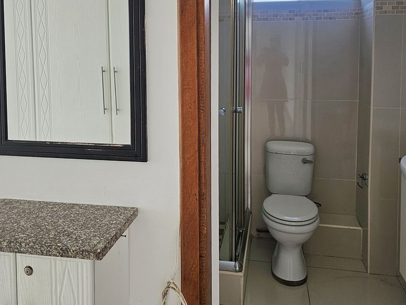 A functional bathroom featuring a shower enclosure, toilet, and vanity unit with a granite countertop, finished with neutral wall and floor tiles.