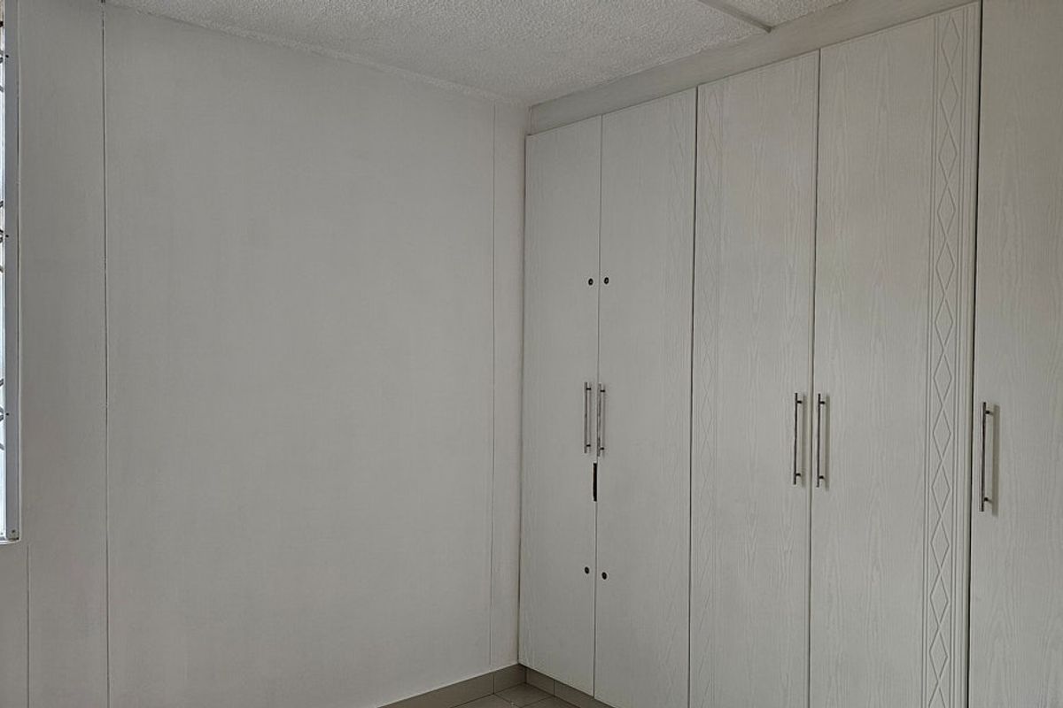 A clean, empty bedroom featuring neutral walls, tiled flooring, and ample built-in cupboard storage with security bars on the window.
