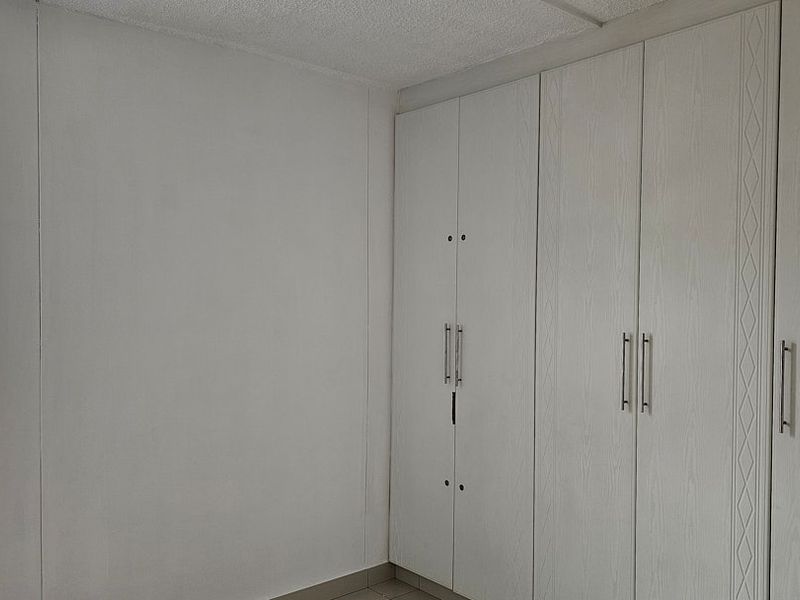A clean, empty bedroom featuring neutral walls, tiled flooring, and ample built-in cupboard storage with security bars on the window.